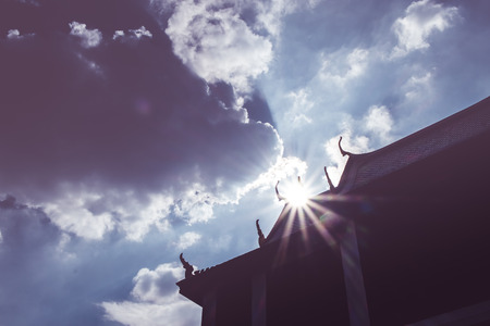 silhouette photo of Thai roof with sun beam over rooftop with sky and cloudの写真素材
