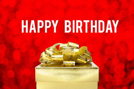 Close up Golden present  with big bow and Happy Birthday word at red bokeh blur background.の写真素材