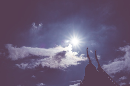 silhouette photo of Thai roof with sun beam over rooftop with sky and cloudの写真素材