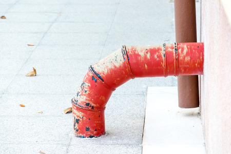 Rustic red waste tube from building to floor.の写真素材