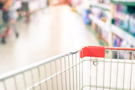 Supermarket store blurred background with close up shopping cart and bokeh light.の写真素材