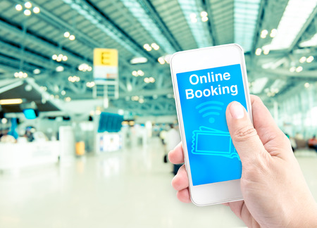 Hand holding mobile with online booking with blur airport background, Digital Booking concept.の写真素材