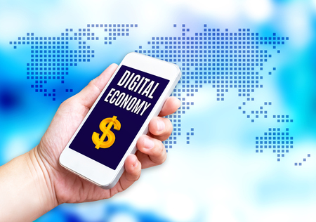 Hand holding mobile phone with Digital economy word with blue blurred background,Digital marketing concept.の写真素材