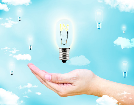 Open female hand with floating glowing lightbulb with blue sky and cloud, Creative idea concept.の写真素材
