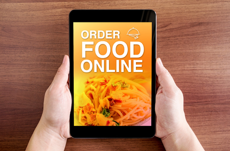 Two hand holding tablet with Order food online and icon on screen at dark brown table top,Digital business conceptの写真素材