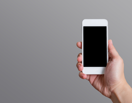 Hand holding blank black screen smart phone (mobile phone) at dark grey background,Mock up for display or montage of your content,Leave space at side of object to adding text.の写真素材