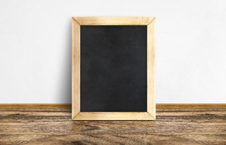 Empty Blackboard leaning at rustic wooden floor and white wall, Template mock up for adding your design and leave space beside frame for adding more text..の写真素材