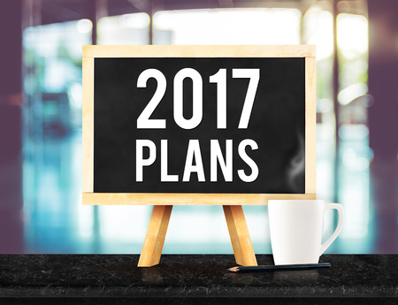2017 plans on blackboard with easel on black marble table with coffee cup and pencil on blurred building hall way background,New year business plan concept.の写真素材