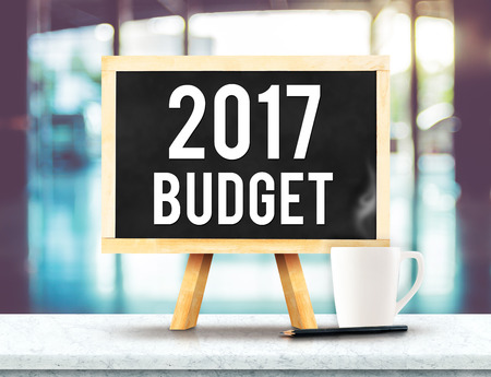 2017 budget on blackboard with easel on black marble table with coffee cup and pencil on blurred building hall way background,New year business plan concept.の写真素材
