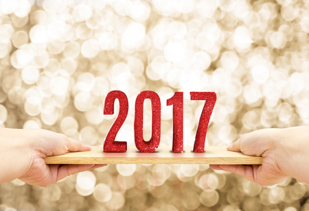 Hand holding wood plate with 2017 Happy new year red glitter number at blur golden sparkling bokeh light background,Holiday concept .の写真素材