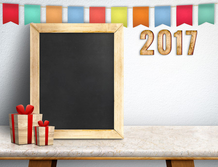 Happy new year on blackboard with gift and colorful flag banner on marble table at white wall,Leave...
