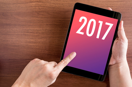 Hand touch tablet with 2017 year number on screen on wood table,Digital happy new year card, Leave...