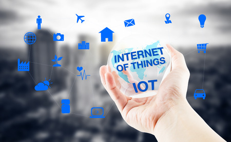 Hand holding clear transparent ball with Internet of things (IoT) word with world map and city blur background, Digital Marketing conceptの写真素材
