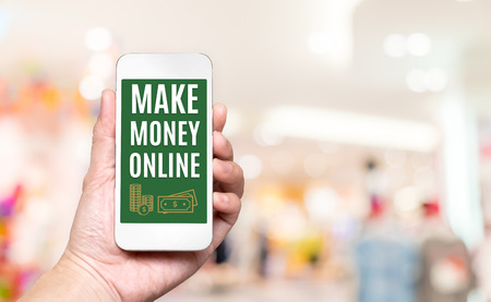 Hand holding mobile with Make money online word on screen with blur shopping mall background,Digital business concept.の写真素材