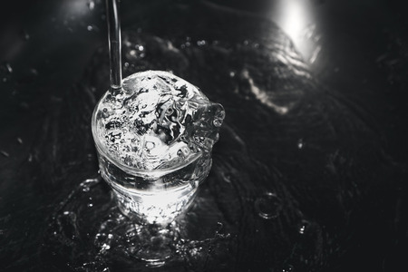 Pouring water from tap to glass on stainless steel stand at kitchen,dark tone filtered.の写真素材