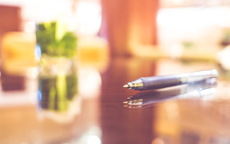 Close up pen on glass table top with blur meeting room background.の写真素材