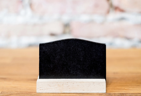Blank blackboard on wood table top at blur brick background in restaurant,Mock up for display or montage of text.の写真素材