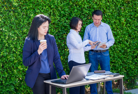 Businesswoman working outside office with team at green leaf wall,business on go and using digital technology device to corporate workflow.の写真素材
