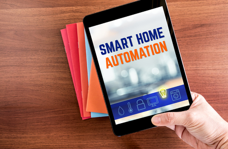 Top view of hand holding tablet with smart home automation word with icon over color notebook on wooden table top,Internet of things conceptの写真素材