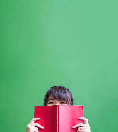 Happy young teenager girl holding red book cover face with thinking action against green vivid wall,Leave copy space upper head to adding content of design for advertising education campaign concept.の写真素材