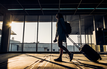 Silhouette of young girl walking with luggage walking at airport terminal window at sunrise time,travel concept,journey lifestyle.の写真素材