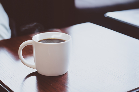 Close up hot black coffee cup on wood table top at coffee shop window.の写真素材