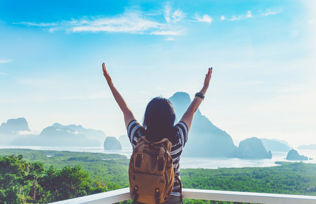 Happy young traveler woman backpacker raised arm up to sky enjoying a beautiful of nature at top of mountain view point and sea,Freedom wanderlust,Khao Samed Nang Chee Viewpoint,Phang Nga,Thailand.の写真素材
