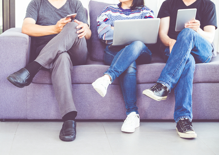 Group of friends sitting at cough and having fun and using digital device (mobile,laptop,tablet) at...