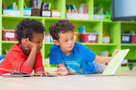 Two boy kid lay down on floor and reading tale book  in preschool library,Kindergarten school...