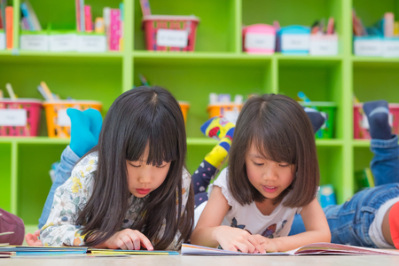 Two girl kid lay down on floor and reading tale book  in preschool library,Kindergarten school education concept.の写真素材