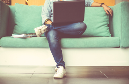 Close up young adult using laptop computer and sitting at green sofa at home,relaxing lifestyle,vintage filter.の写真素材