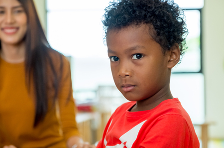 African American ethnicity kid with teacher smiling at background in kindergarten classroom.の写真素材