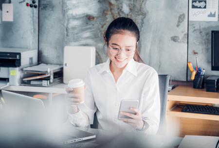 Asian businesswoman take a coffee break after working at laptop computer on desk with smiling face,Happy office life concept,working woman at modern home office.の写真素材