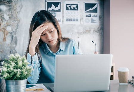 Stressed Asian creative designer woman cover her face with hand and feel upset from work in front of laptop computer on desk at office,Stress office lifestyle concept.の写真素材