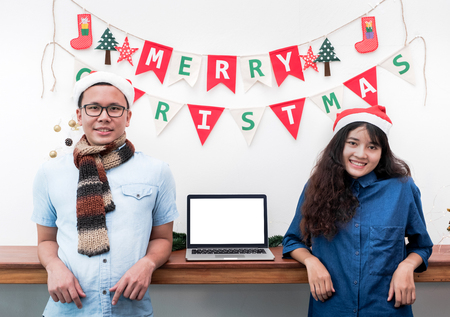 smiling Lover couple standing at Christmas garland on wal with with laptopl,Mokc up template blank screen computer for display of design,Holiday celebration promotion conceptの写真素材