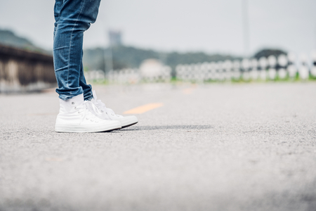 Close up woman wear jean and white sneaker standing on highway road in sunny day,Alone travel or solo traveler concept.の写真素材