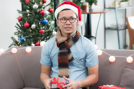 Asia man holding small gift box and looking at friend feel envious of other bigger present and sit alone on sofa,jealous and lonely emotionの写真素材