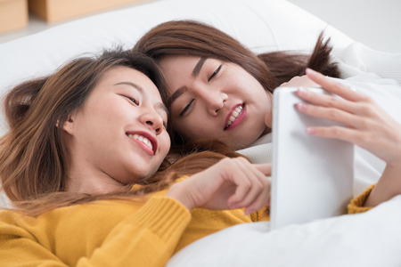 Asia lgbt couple lying on bed using tablet together in bedroom with happiness moment together,love wins concept.の写真素材