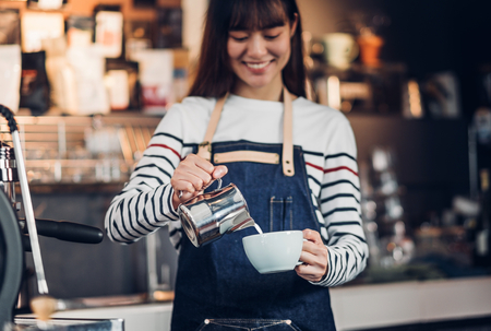 Asia woman barista pour milk into hot coffee cup at counter bar in front of machine in cafe restaurant,Food business owner conceptの写真素材