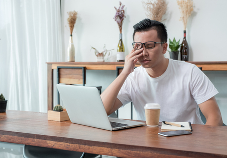 asia casual man cover face with hand upset from work in front of laptop computer in coffee shop,stress emotion concept,work outside office,work at homeの写真素材