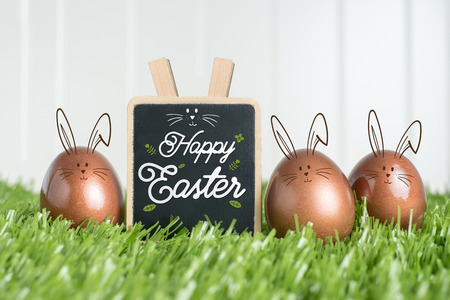 Happy easter with doodle rabbit on blackboard and rose gold color easter eggs on green grass field...