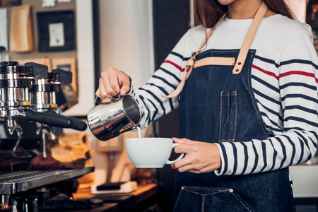 Asia woman barista pour milk into hot coffee cup at counter bar in front of machine in cafe restaurant,Food business owner conceptの写真素材