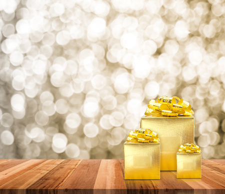 Golden present on wood table top with blur sparkling gold bokeh light background,Gift giving concept,Leave space for adding text for new year or Christmas cardの写真素材