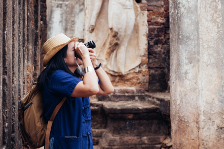Asian tourist woman taking photo of ancient of Thai temple architecture at Sukhothai Historical Park,Thailand. Female traveler in casual thai Mauhom shirt style visiting city.Summer holiday vacationの写真素材