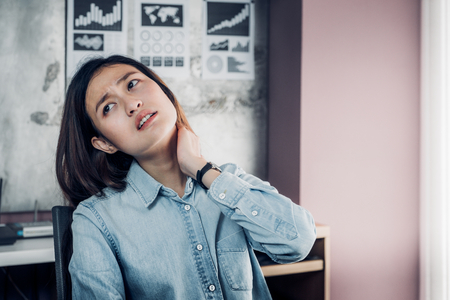 office syndrome,Asian designer neck ache when working,use hand catch her neck pain from hard working long time in front of laptop computer on desk at office, home office lifestyleの写真素材
