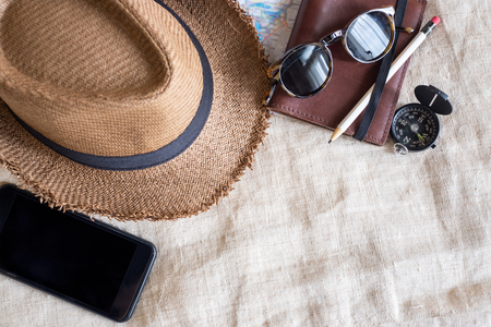 Top view of Summer brown panama straw hat,mobile,sunglasses,notebook map,compass on linen cloth.vacation travel concept.copy space for adding textの写真素材