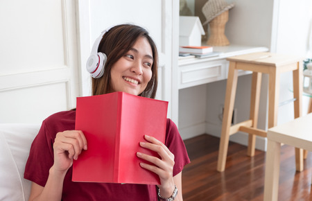 Asian woman listening music on headphone and reading book with relax pose at couch in living room at home.leisure lifestyleの写真素材