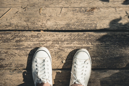 Aerial view of white sneakers canvas shoe stand on grunge old wood floor and tree shadow in sunny day, Leave space on top for adding your textの写真素材