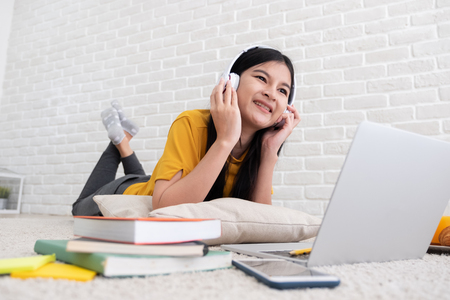 Asian female listen to music and use laptop computer to work at home.woman lay down on carpet at brick wall.working online lifestyleの写真素材