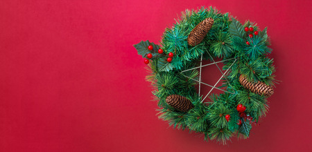Green pine christmas wreath with star and pine cone ,cherry decoration item on red wall background.copy space for adding text or design.Celebration holiday festive greeing cardの写真素材
